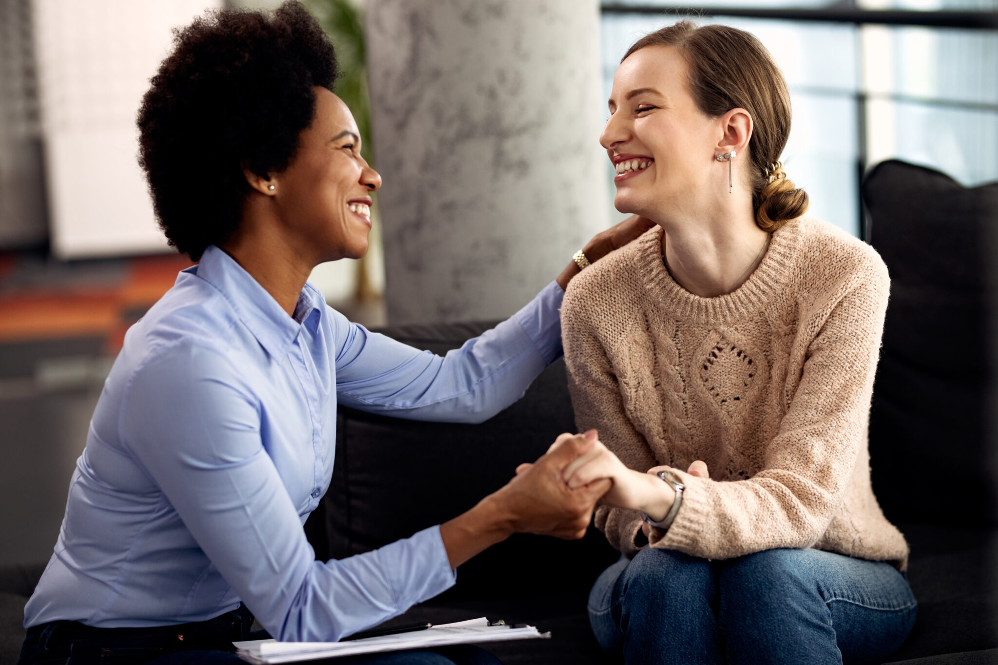 Young happy woman holding hands with her psychotherapist during an appointment at the clinic.