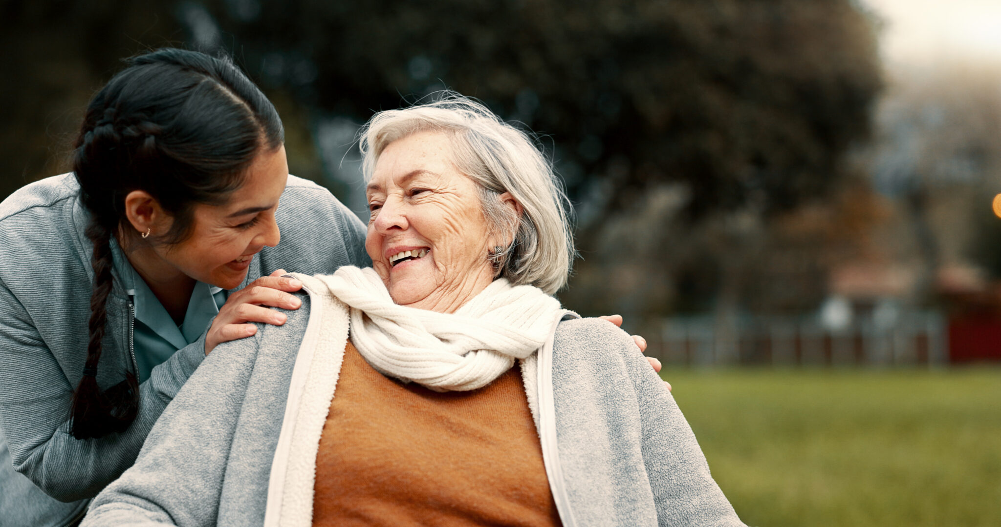 Caregiver helping woman with disability in park for support, trust and care in retirement. Nurse talking to happy senior patient in wheelchair for rehabilitation, therapy and conversation in garden.