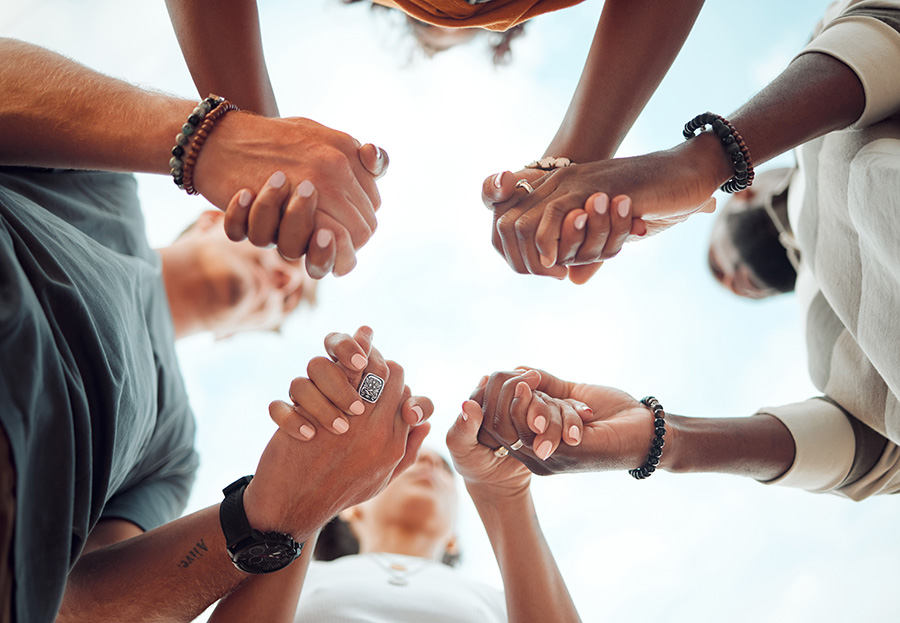 Holding hands, support and friends praying for spiritual growth, community and gratitude together with sky from below. Group of people in partnership for hope, love and human faith in connection