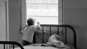 A young resident of Monroe Hall, a children's residence at Clover Bottom, peers out a window beside his bed in the ward July 18, 1972. He spends much of each day at his bed with little to occupy his time.